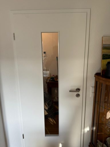 Weiße Tür mit vertikalem Fenster, das den Raum dahinter sichtbar macht.