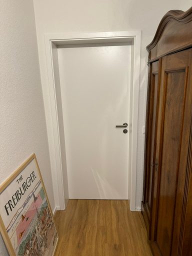 Weiße Tür in einem Flur mit Holzfußboden und antikem Schrank daneben.